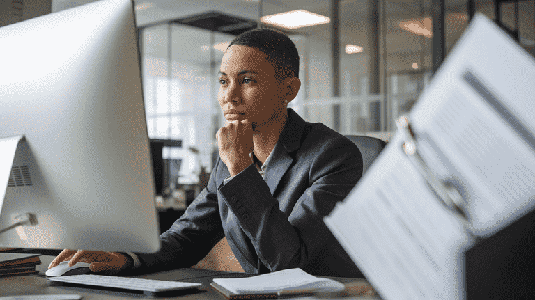 A professional sitting at an office desk, thoughtfully considering their computer screen with legal documents nearby, symbolizing the impact of criminal charges on employment.