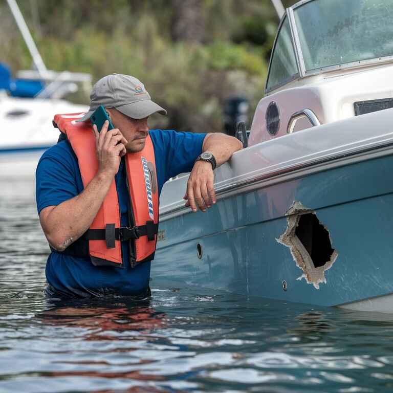 A boater calling for help while inspecting damage to a vessel after a collision